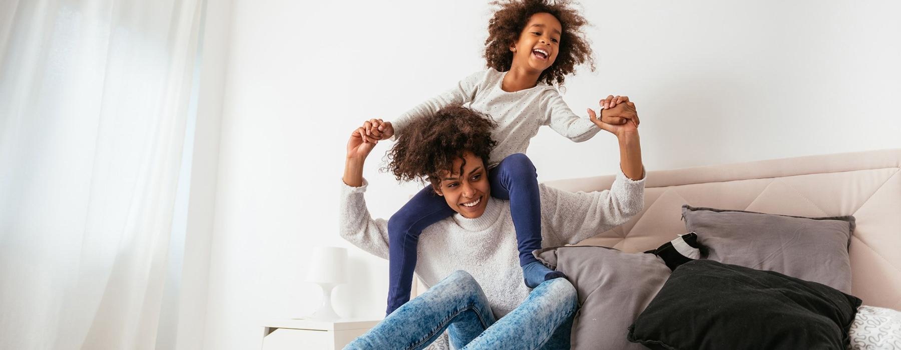 mother and daughter happily play on a large bed